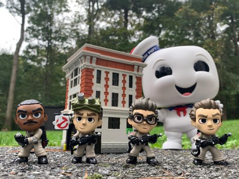Funko Pops of the original four Ghostbusters standing in front of the firehouse with Stay Puft looming in the background.